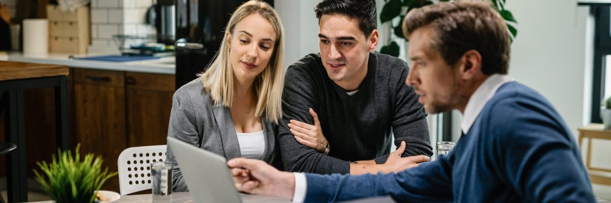 Young couple and real estate agent using laptop while going through housing plan on a meeting.